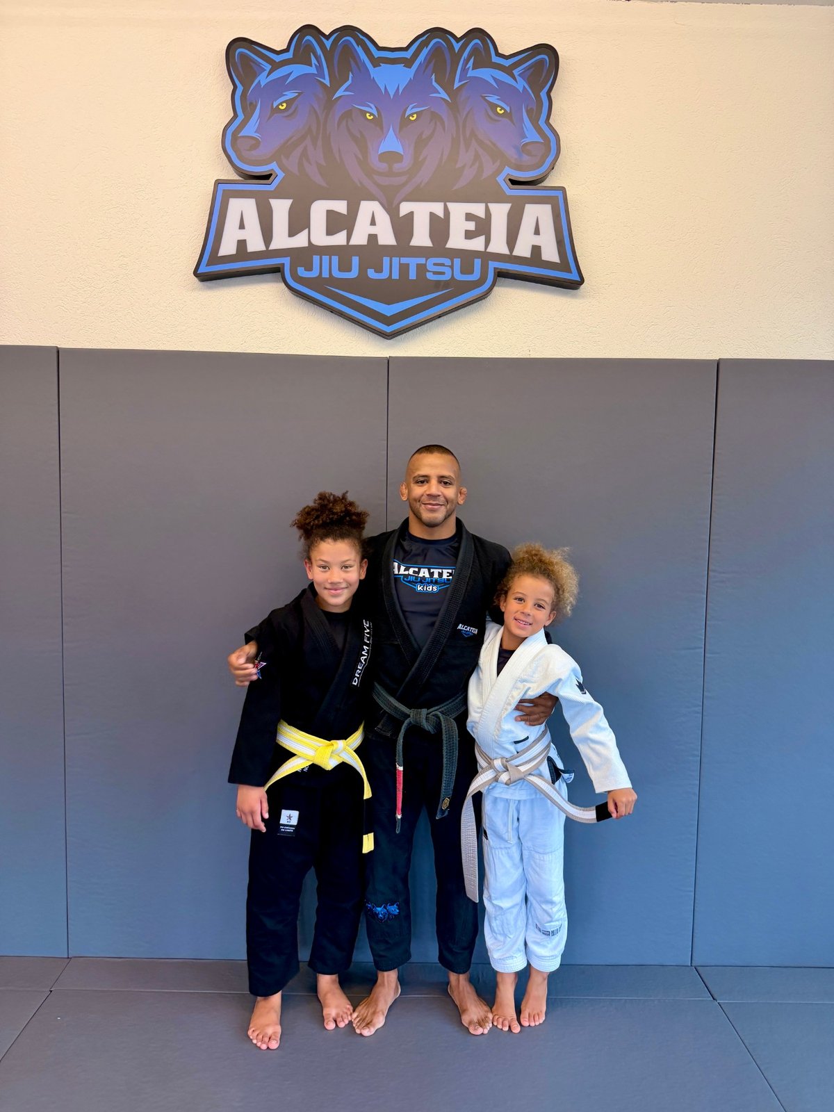 Aleyna im hellblauen Gi mit ihrem grau-weissen Gurt bei Alcateia Jiu Jitsu, neben ihrer Schwester und ihrem Trainer.